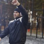 Handsome man in headphones doing stretching exercise while listening music in winter park outdoors